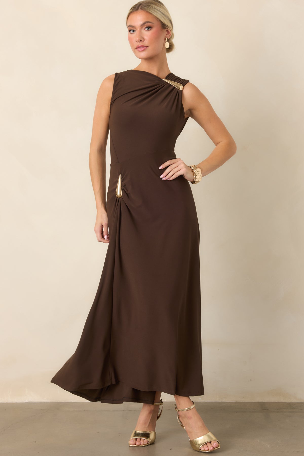 Sculptural dress design featuring a fitted bodice, asymmetrical neckline, and gold-tone teardrop hardware.