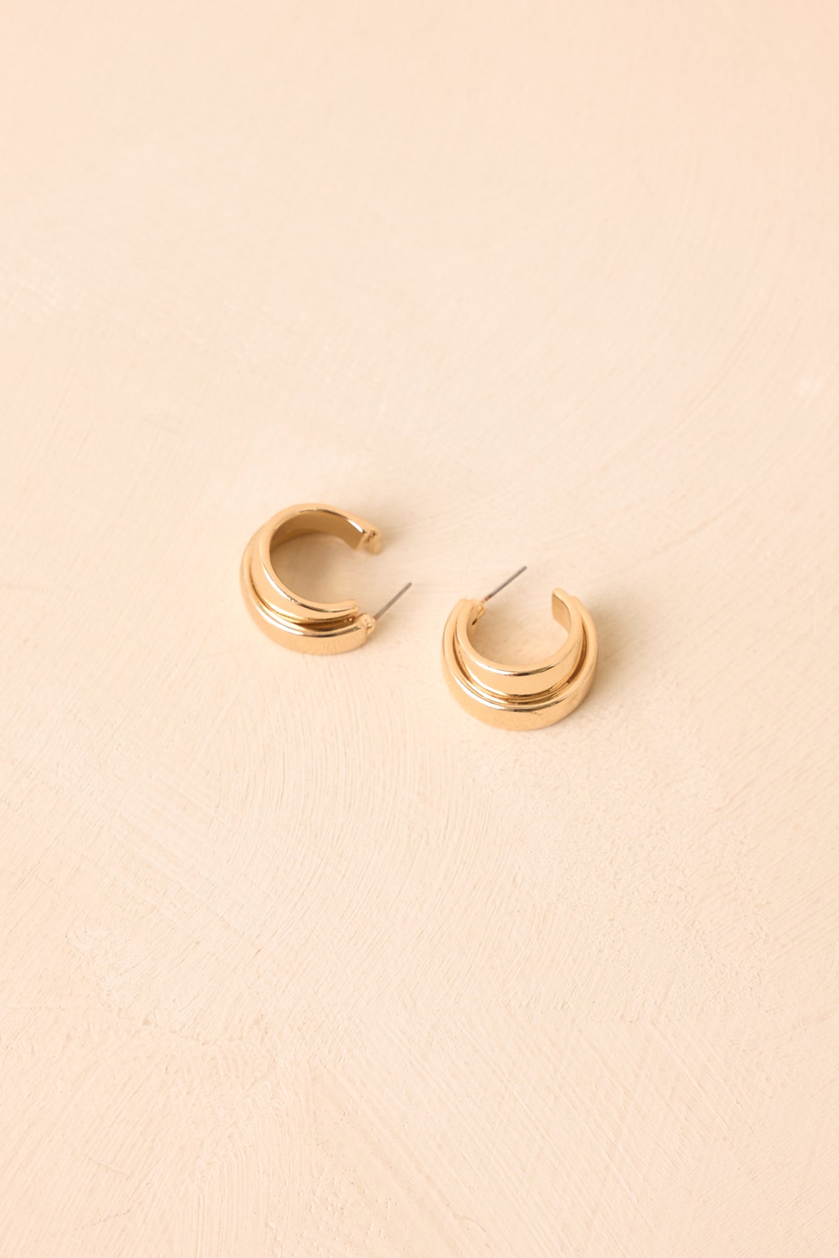 Sculptural gold-tone earrings showcasing a bold curved shape with polished surfaces and dimensional detailing.