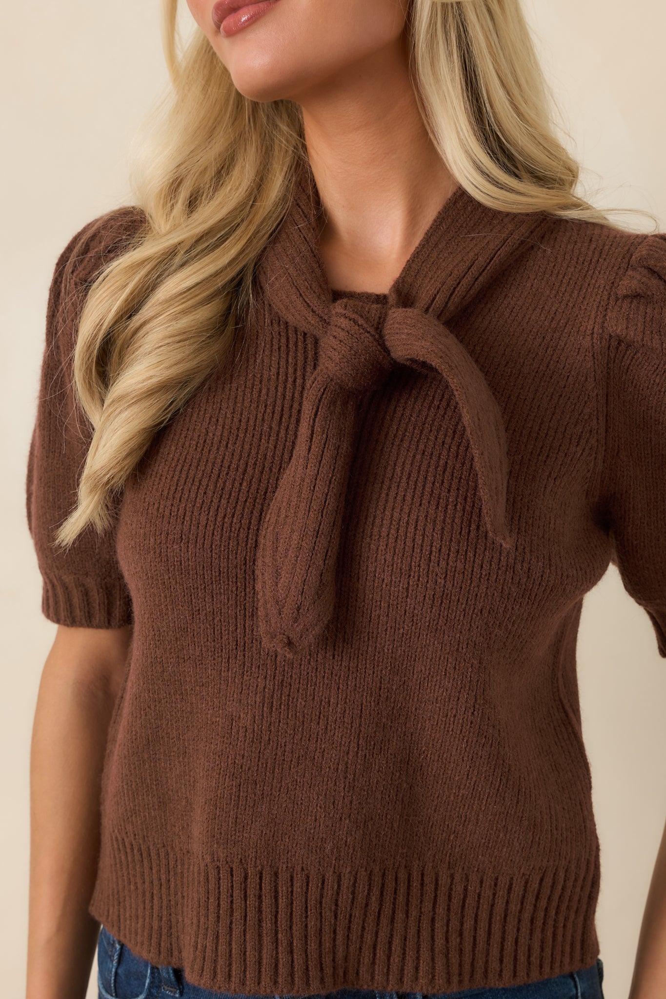 Close-up of the ribbed knit top featuring the oversized self-tie bow neckline and textured fabric detail.