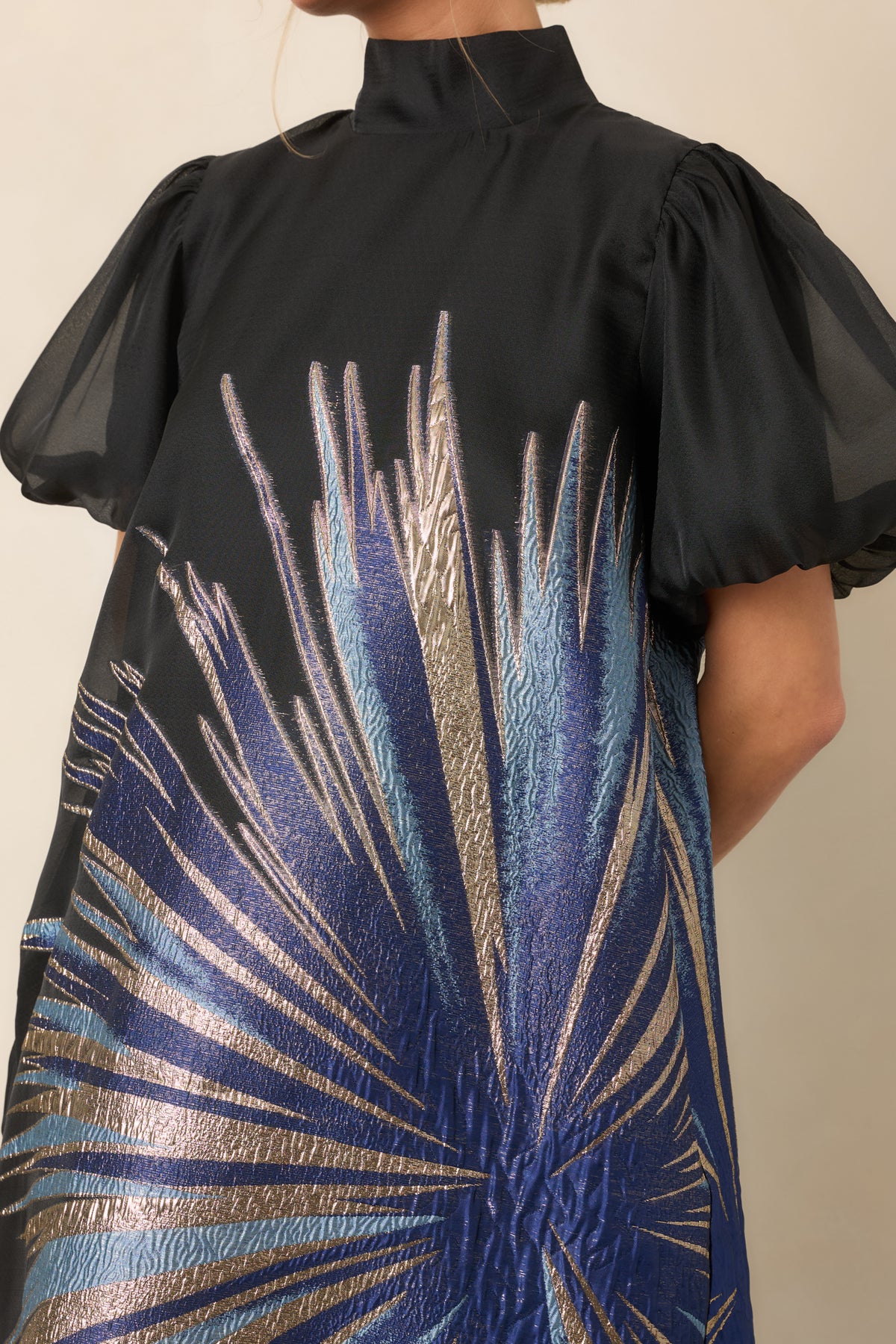 Close detail of the sheer black overlay with shimmering blue and gold metallic starburst detailing.