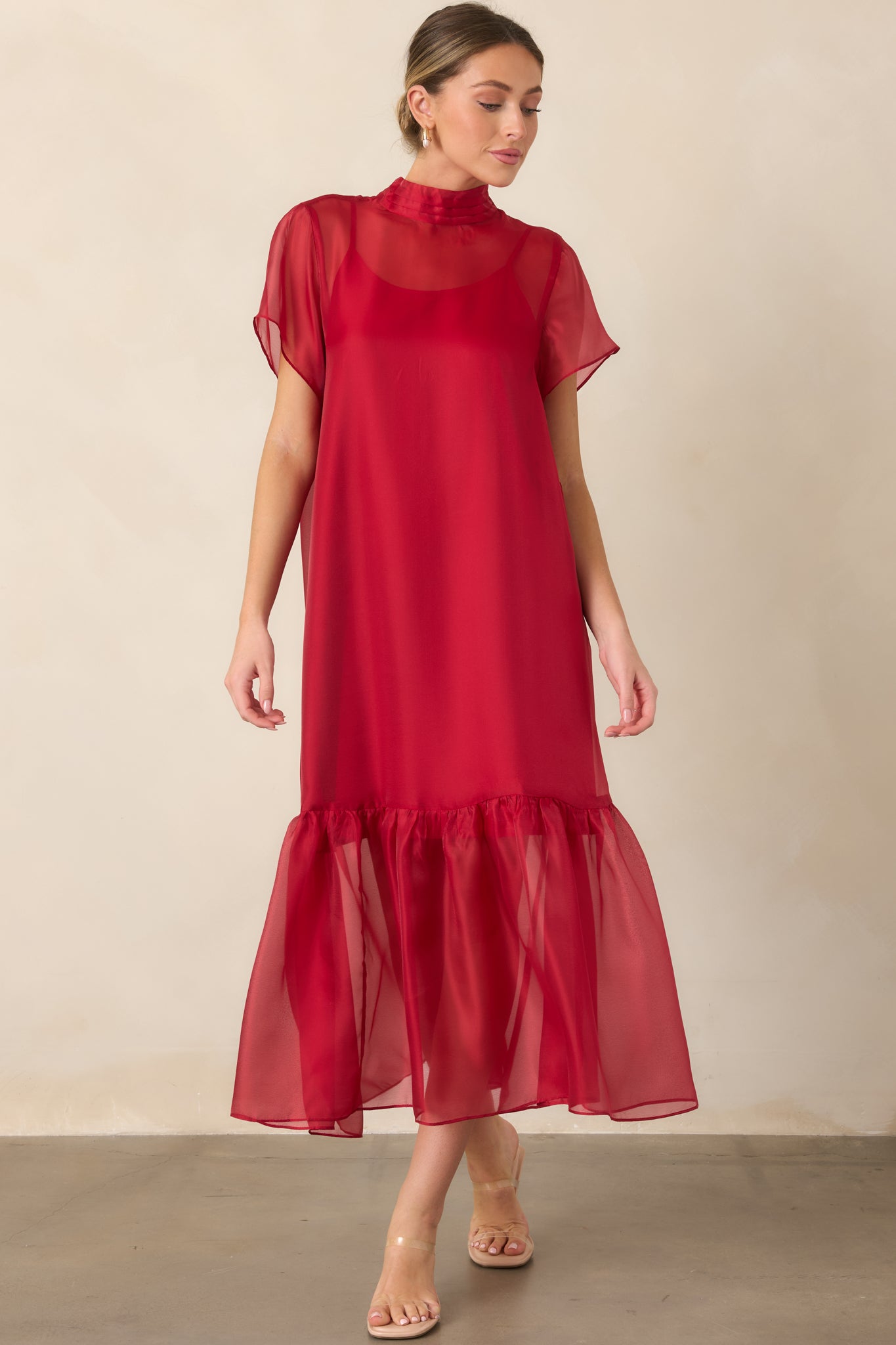 Sheer organza maxi dress with a layered slip lining, pleated mock neckline, short sheer sleeves, and a softly gathered ruffle hem extending to the full length.