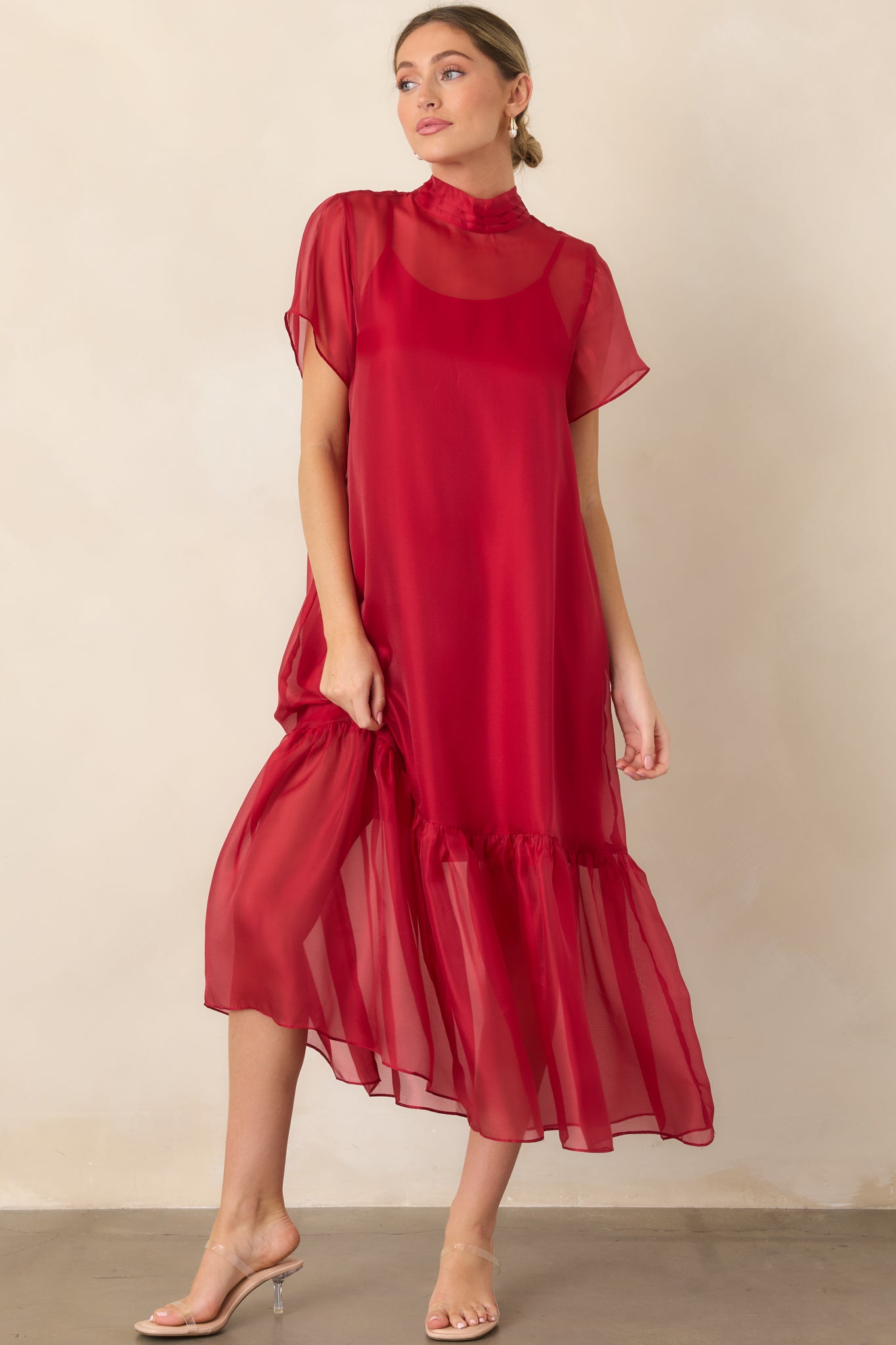 Sheer organza maxi dress featuring a coordinating slip lining, pleated mock neckline, short sheer sleeves, and a gathered ruffle hem.