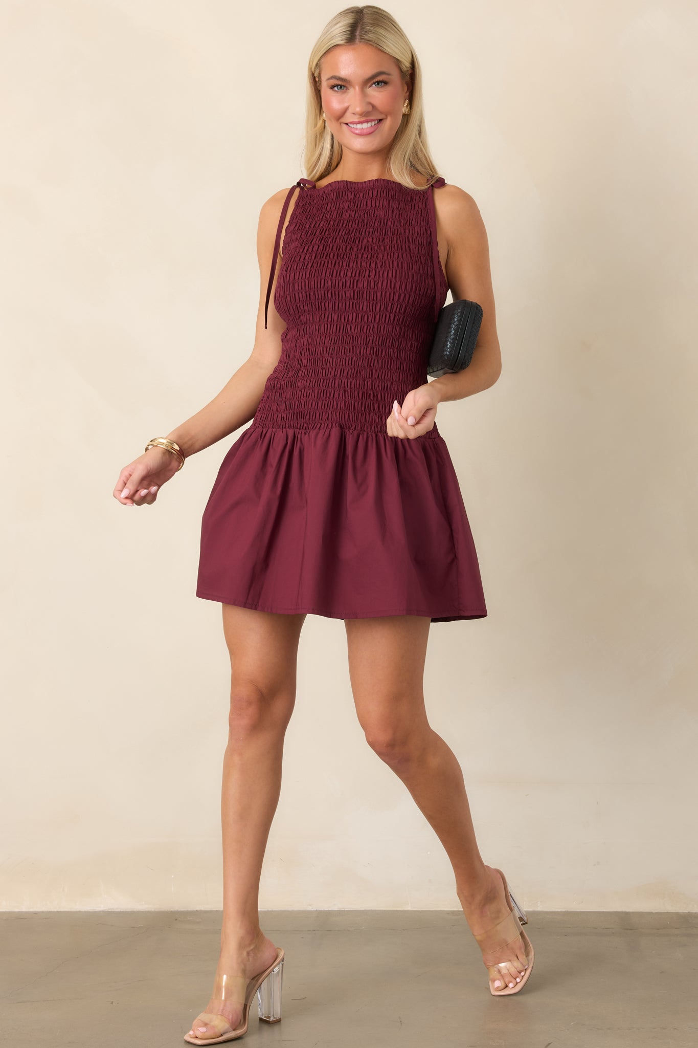Feminine wine red mini dress with a stretchy shirred bodice, adjustable tie straps, flowing gathered skirt, and softly flared hem.