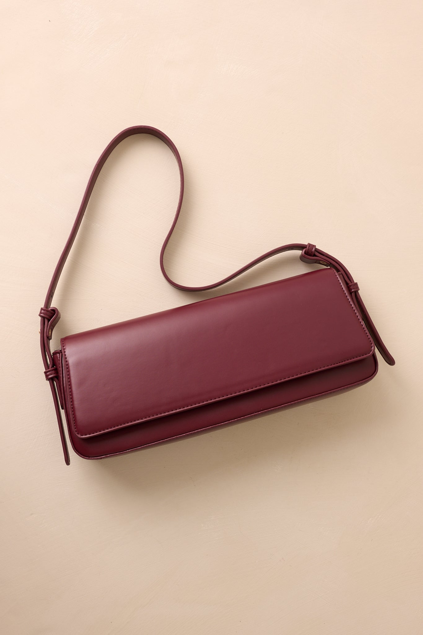 An overhead shot capturing the bag's rectangular shape, adjustable strap, and rich burgundy hue.