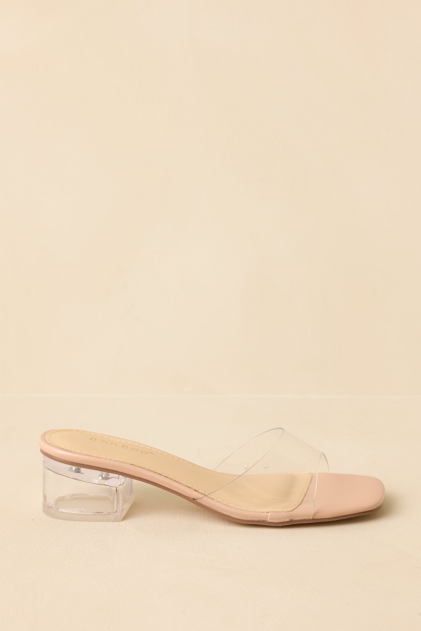 Side angle against a beige background emphasizing the transparent block heel height and shape.