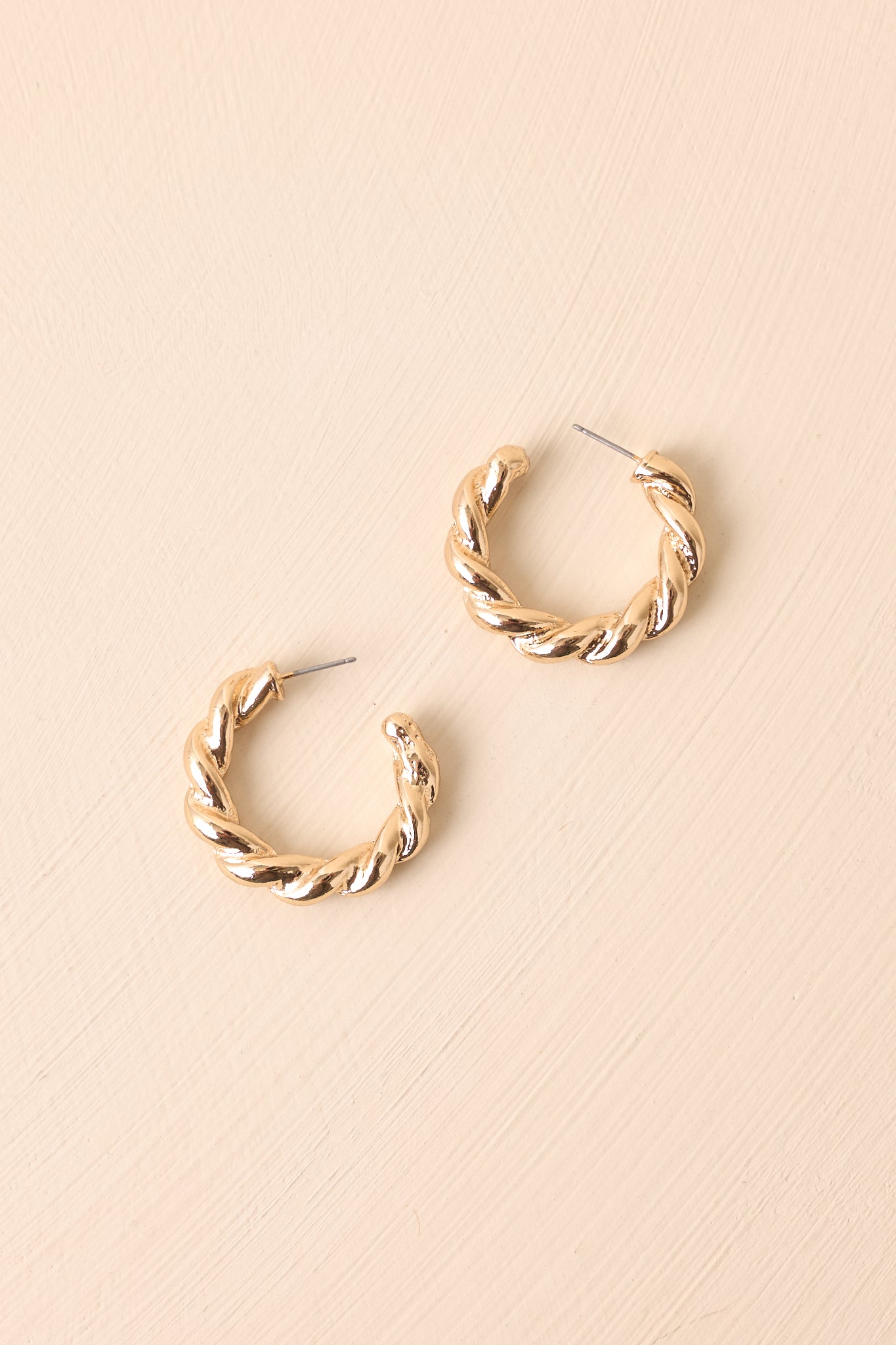 Side angle of the earrings on beige, emphasizing the twisted detail and curved silhouette.