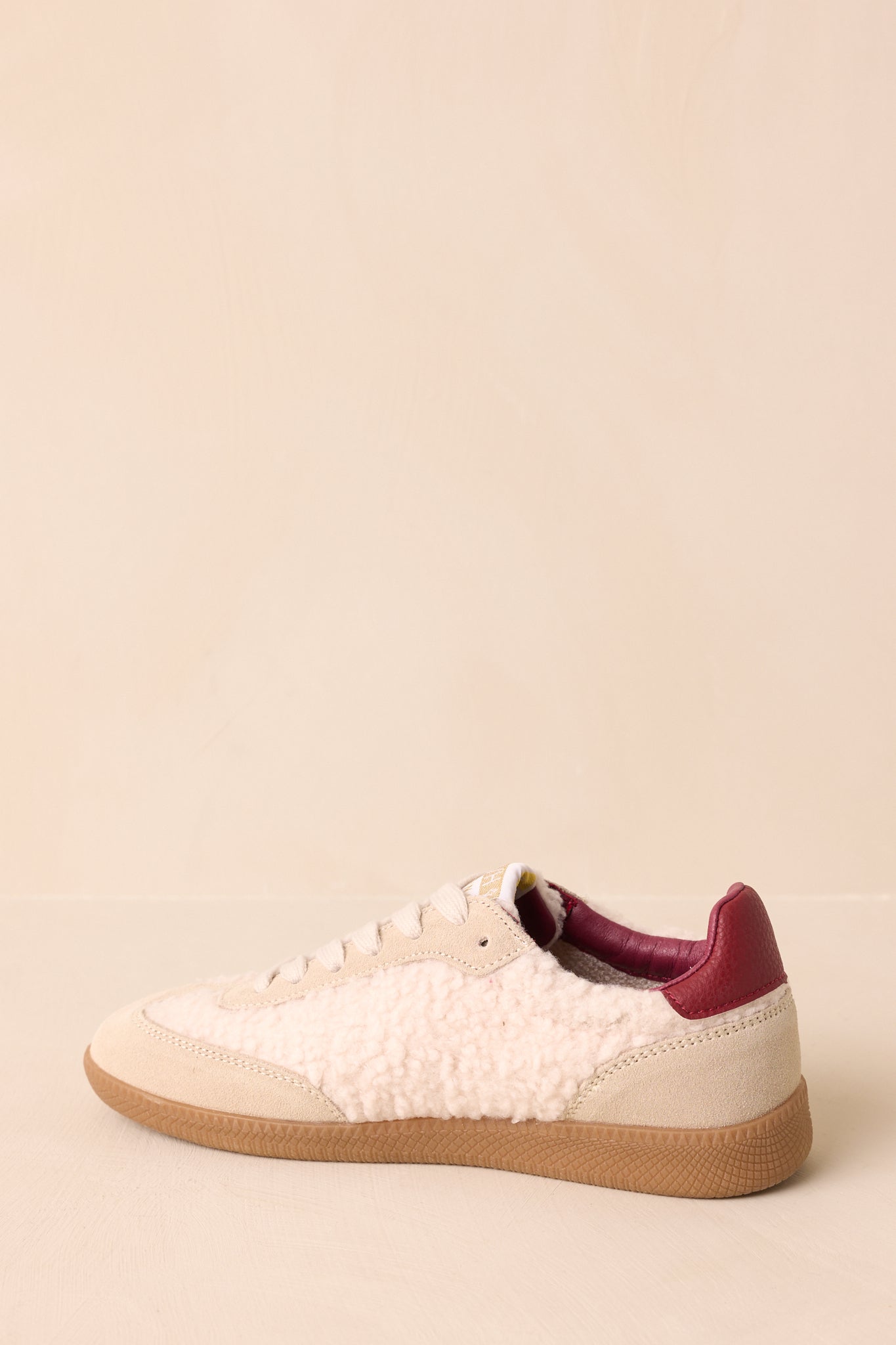 Side profile of low-top sneakers showcasing sherpa and suede panels, bold side logo, and flat brown rubber outsole.