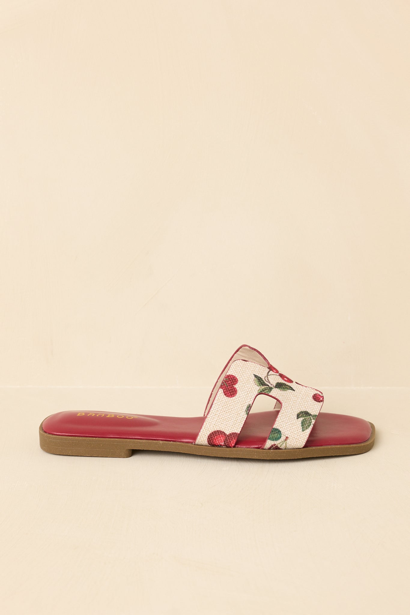 Side profile of fruit print sandals on beige background featuring flat sole and streamlined silhouette
