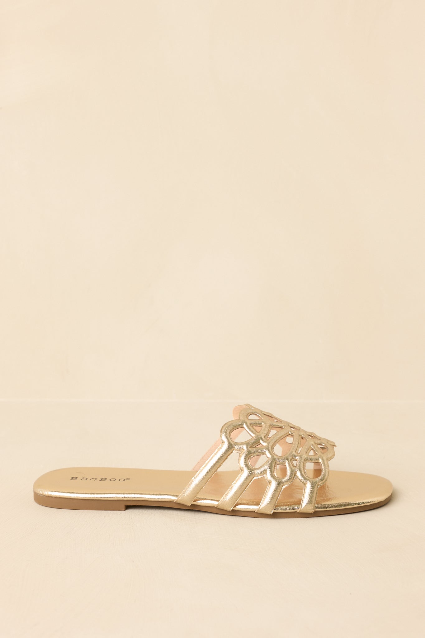Side profile of metallic gold sandals on beige background featuring flat sole and streamlined shape