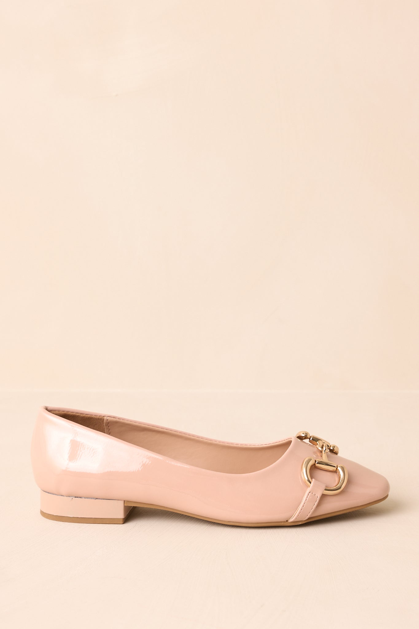 Side profile of beige patent loafers with a clean, structured silhouette and low block heel.