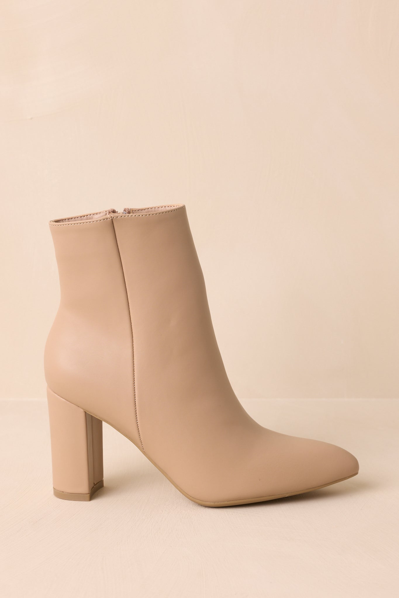 Side view of beige ankle boots showing the sleek pointed toe and structured block heel.