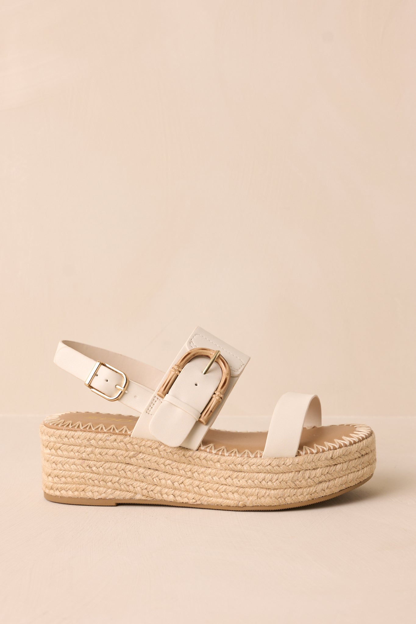 A side view of the ivory sandals, highlighting the woven straw platform wedge heel and elegant gold buckle details.