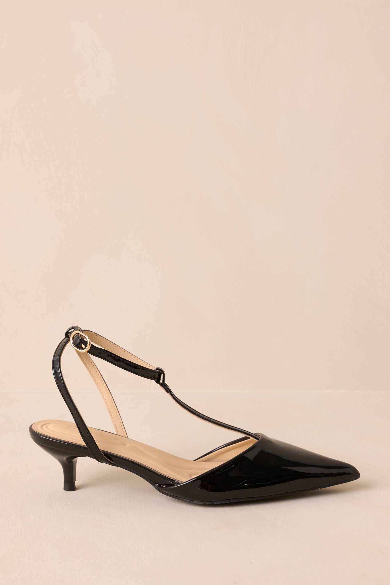 Side view of black T-strap heels with low kitten heel displayed on beige backdrop.
