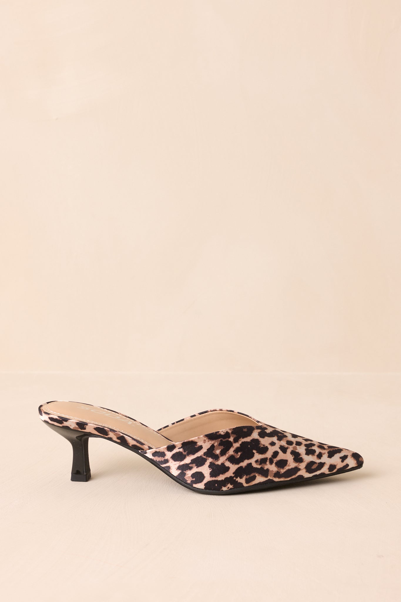 Side view of leopard pointed-toe heels on beige background.