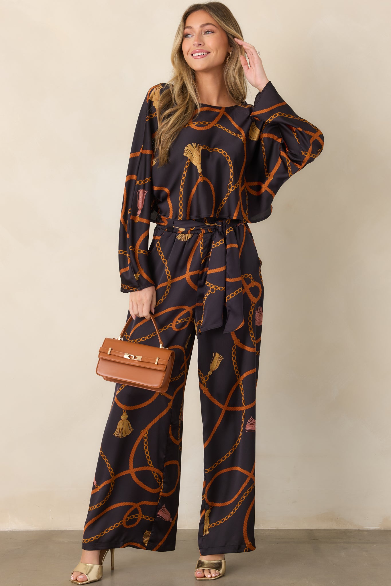 Silky black top with long sleeves, round neckline, and an ornate pattern of ropes, chains, and tassels.