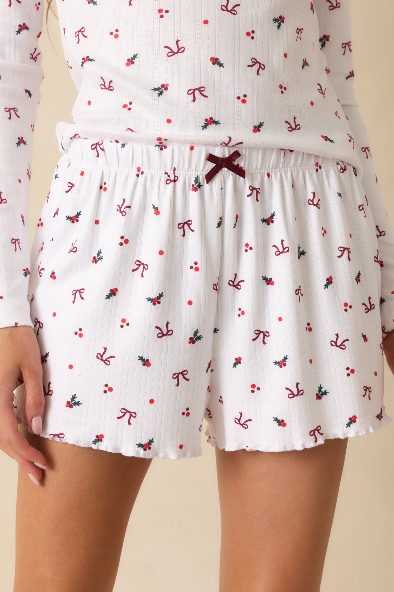 Silky white pointelle fabric with holly-and-bow print, highlighting satin bow detail and elastic high-rise waistband.