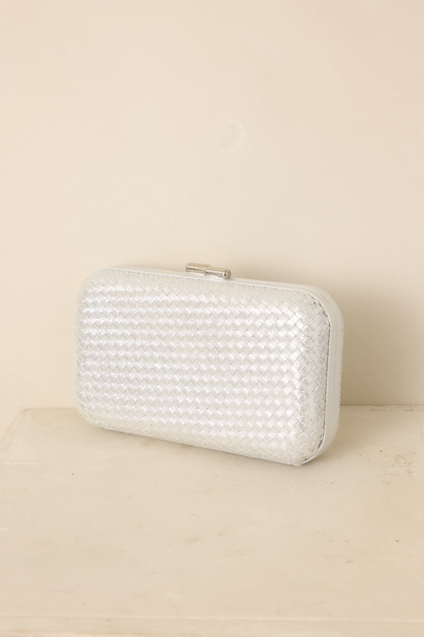 Silver woven clutch featuring a structured rectangular shape, hard case body, rounded edges, and optional chain strap.