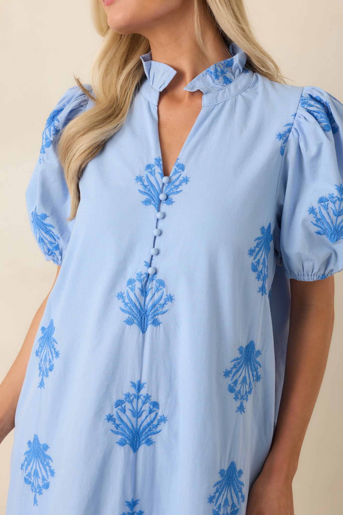Close-up of the sky blue cotton dress featuring tonal embroidery, covered button details, and a softly ruffled neckline.