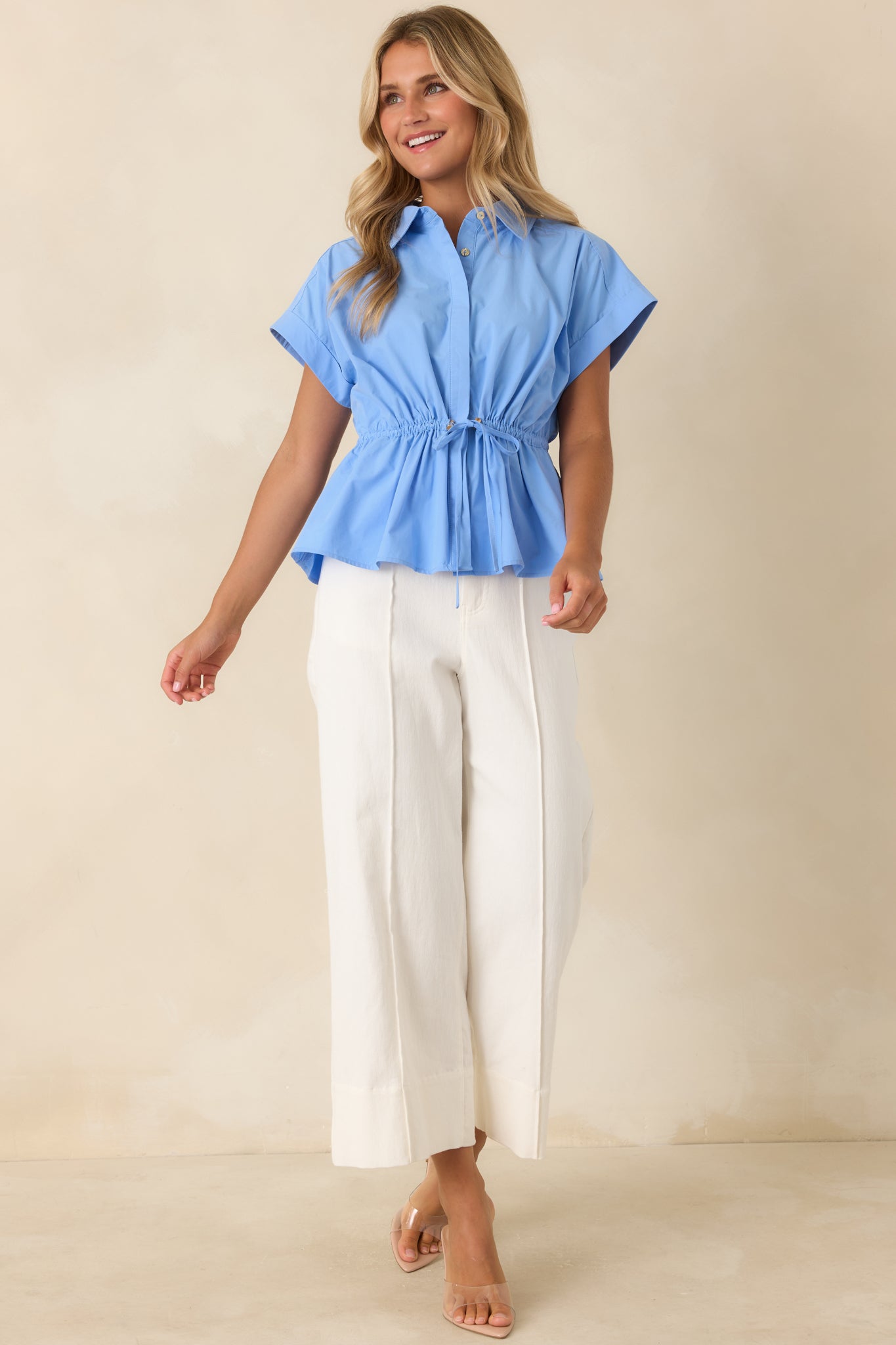 Crisp cotton peplum top in a soft sky blue shade designed with cuffed cap sleeves, a concealed button placket, and an adjustable waist for a flattering silhouette.