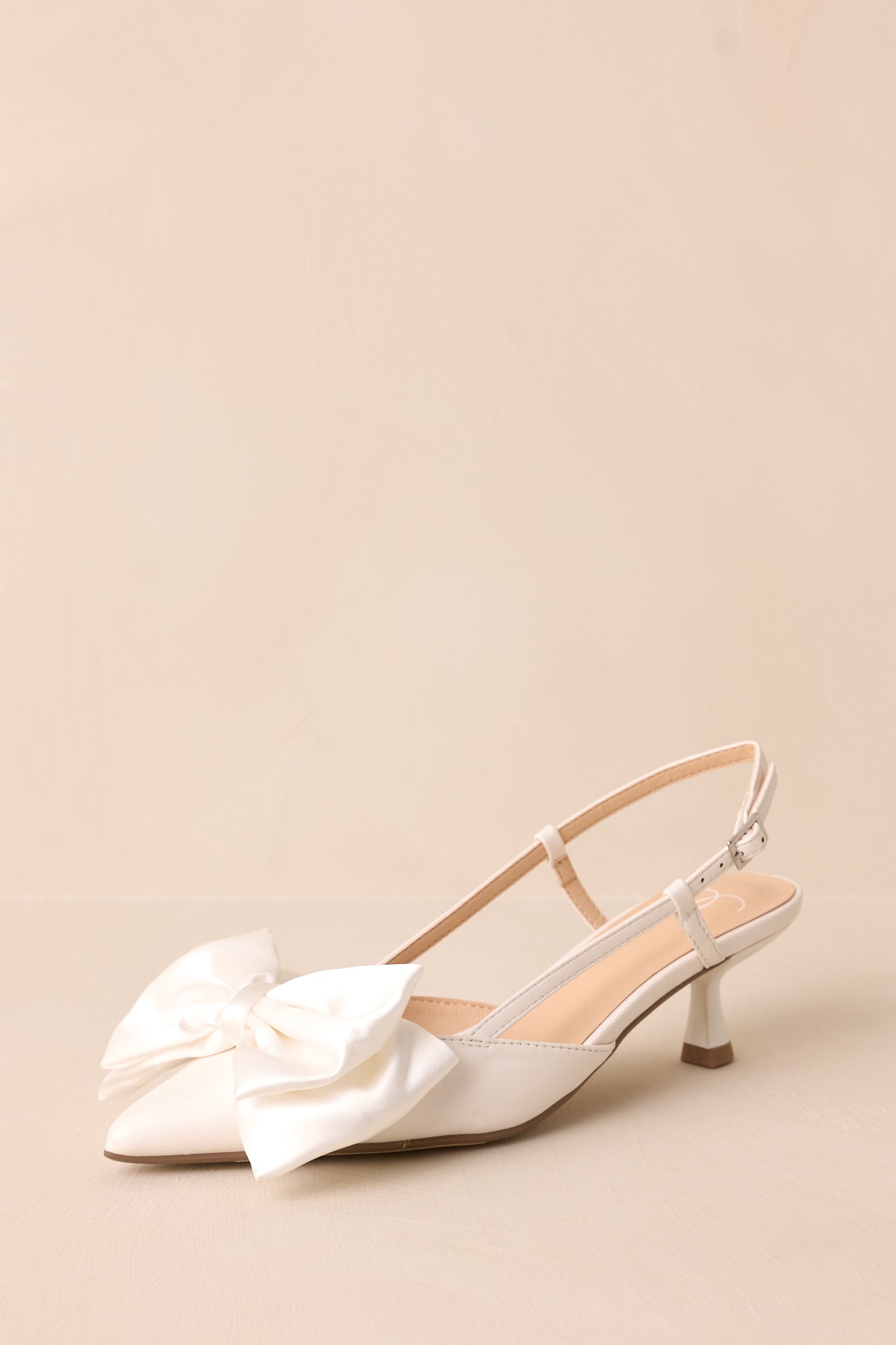 A sleek white heel with a pointed toe and a delicate satin bow for a refined, feminine touch.