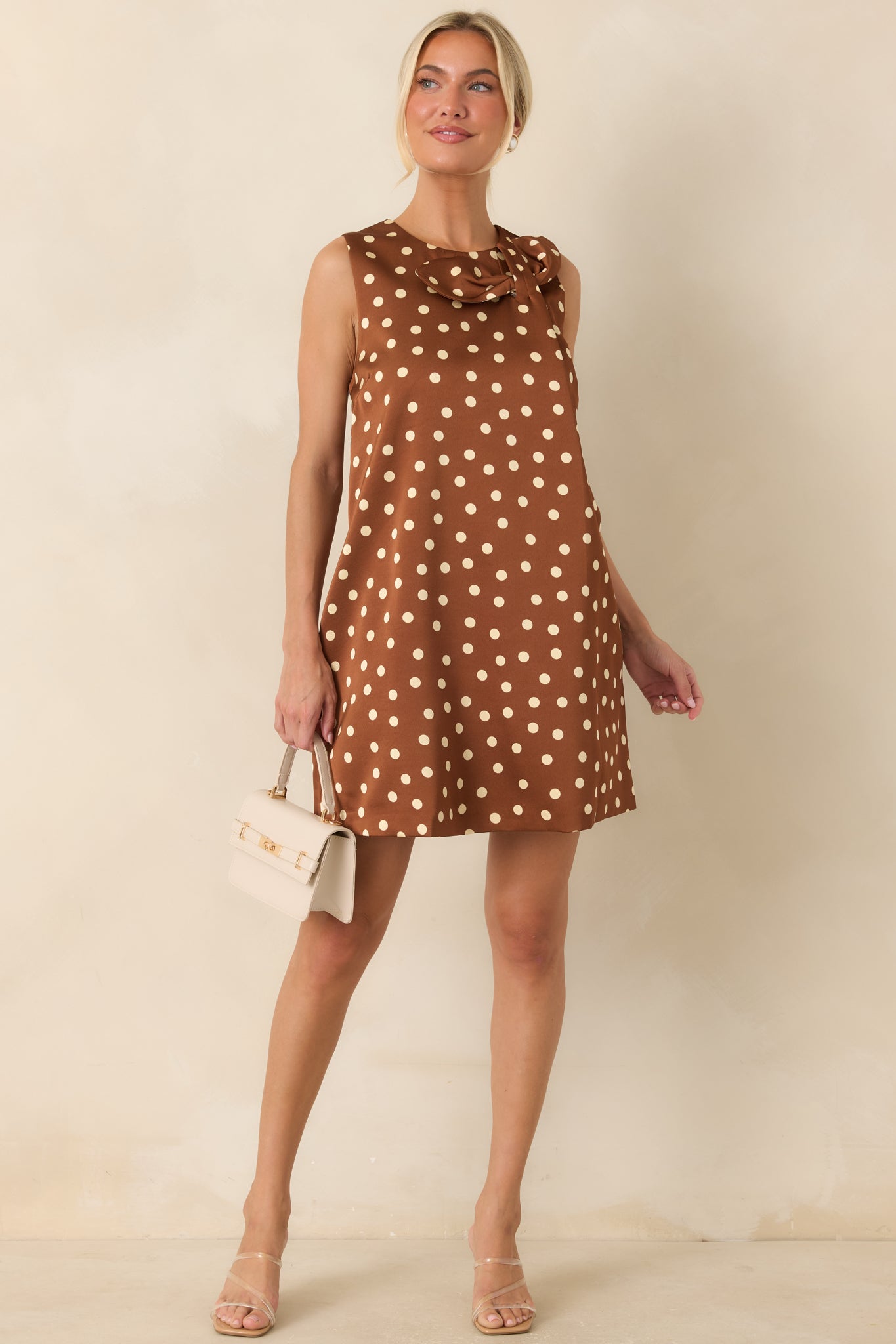 Sleeveless brown mini dress showcasing a vintage-inspired bow neckline, hidden pockets, and a polished silhouette.