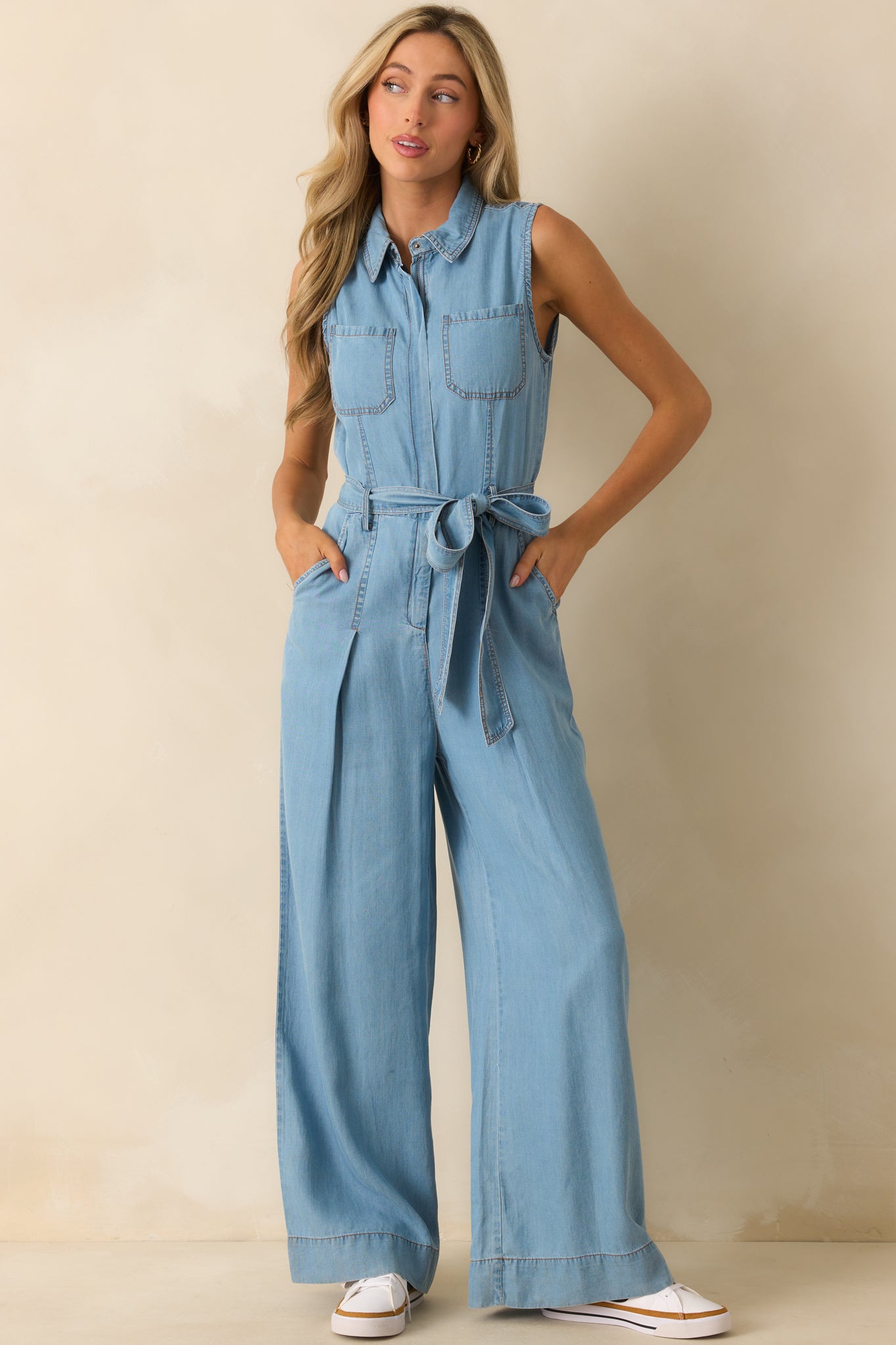 Sleeveless chambray jumpsuit featuring a collared neckline, optional self-tie belt, wide-leg silhouette, and functional front pockets.