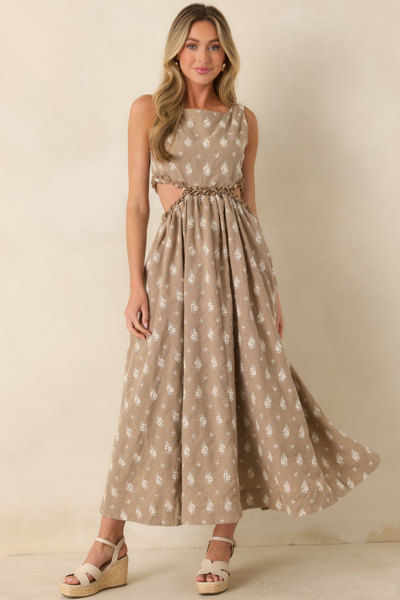 Sleeveless maxi dress showcasing a flowing full-length skirt, soft brown and cream floral eyelet pattern, and modern side cut-out accents.
