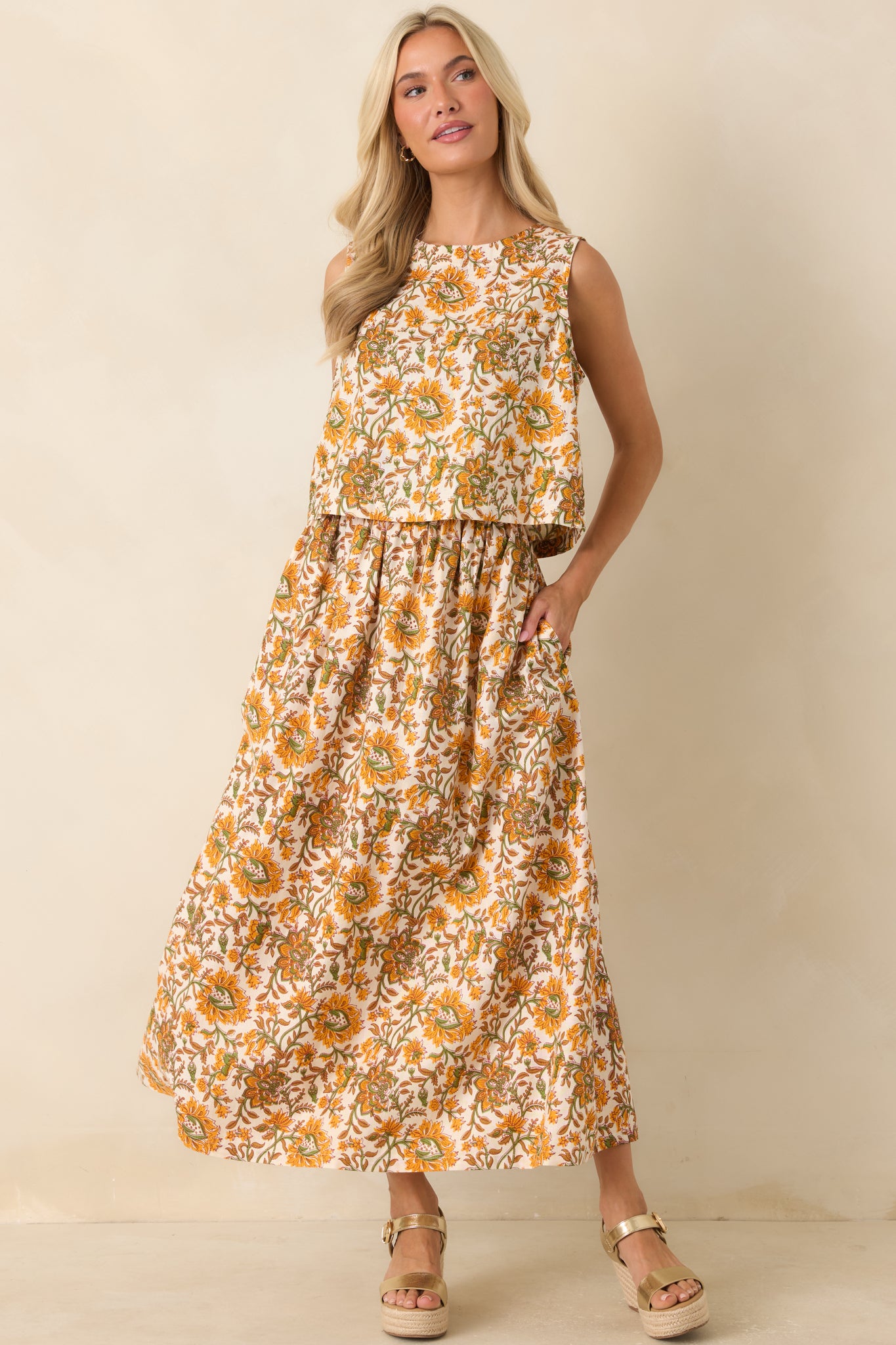 Sleeveless floral top showcasing a high neckline, cropped length, and detailed marigold, olive, and tan pattern on an ivory background.
