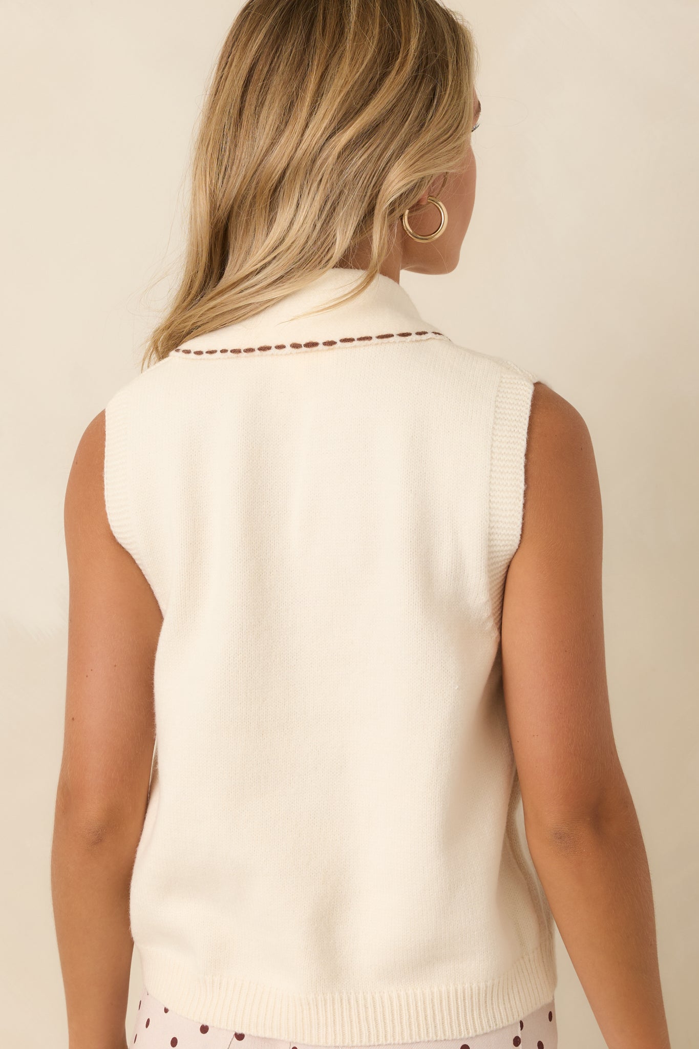 Rear view of the sleeveless knit sweater featuring a smooth back, ribbed hem, and scarf drape.
