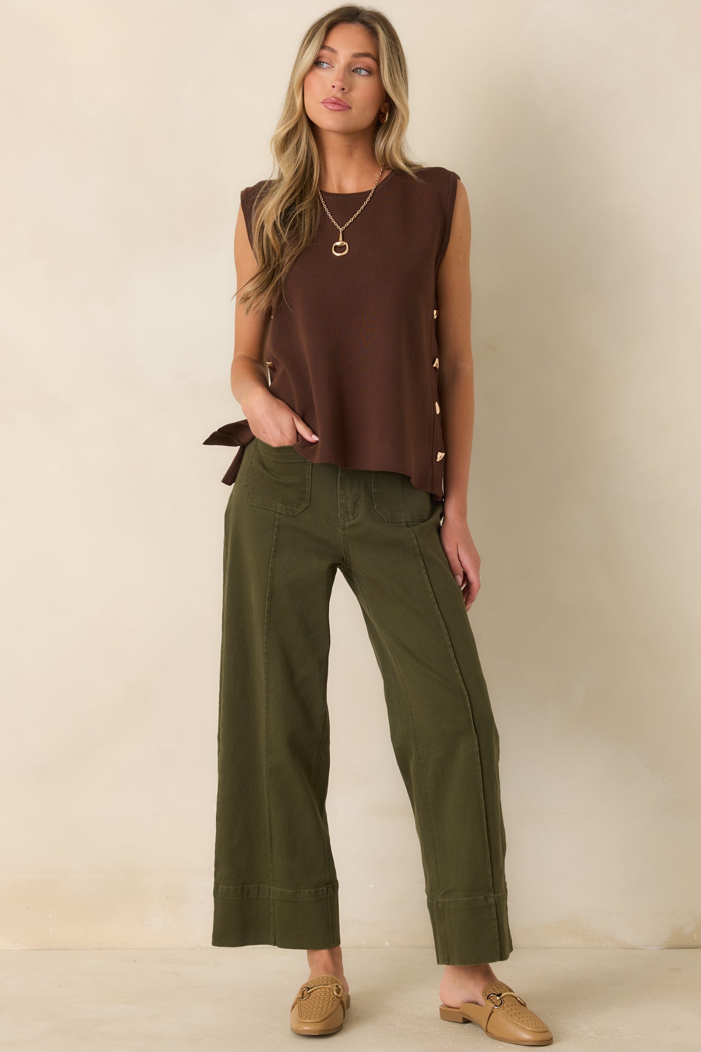 Sleeveless knit sweater featuring a soft drape, minimalist silhouette, and a row of gold-tone buttons for a refined finish.