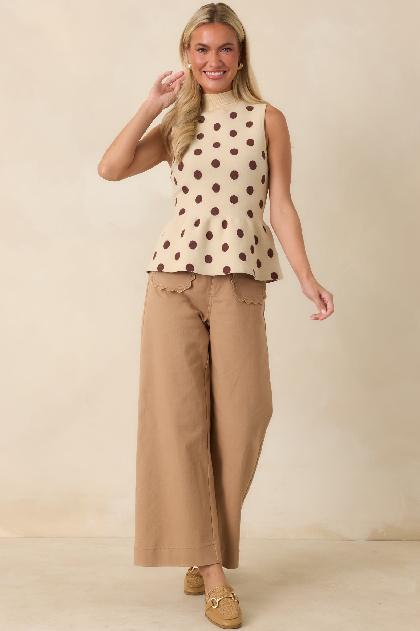Sleeveless knit top with a fitted bodice, playful brown dot pattern, ribbed neckline, and feminine flared peplum shape.