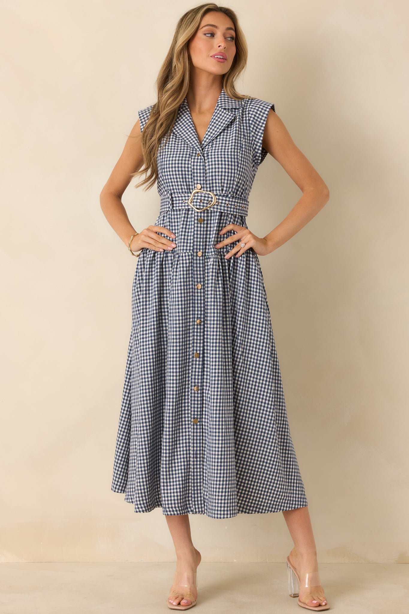 Sleeveless navy gingham midi dress featuring a removable belt with statement buckle, side pockets, and a softly gathered skirt.