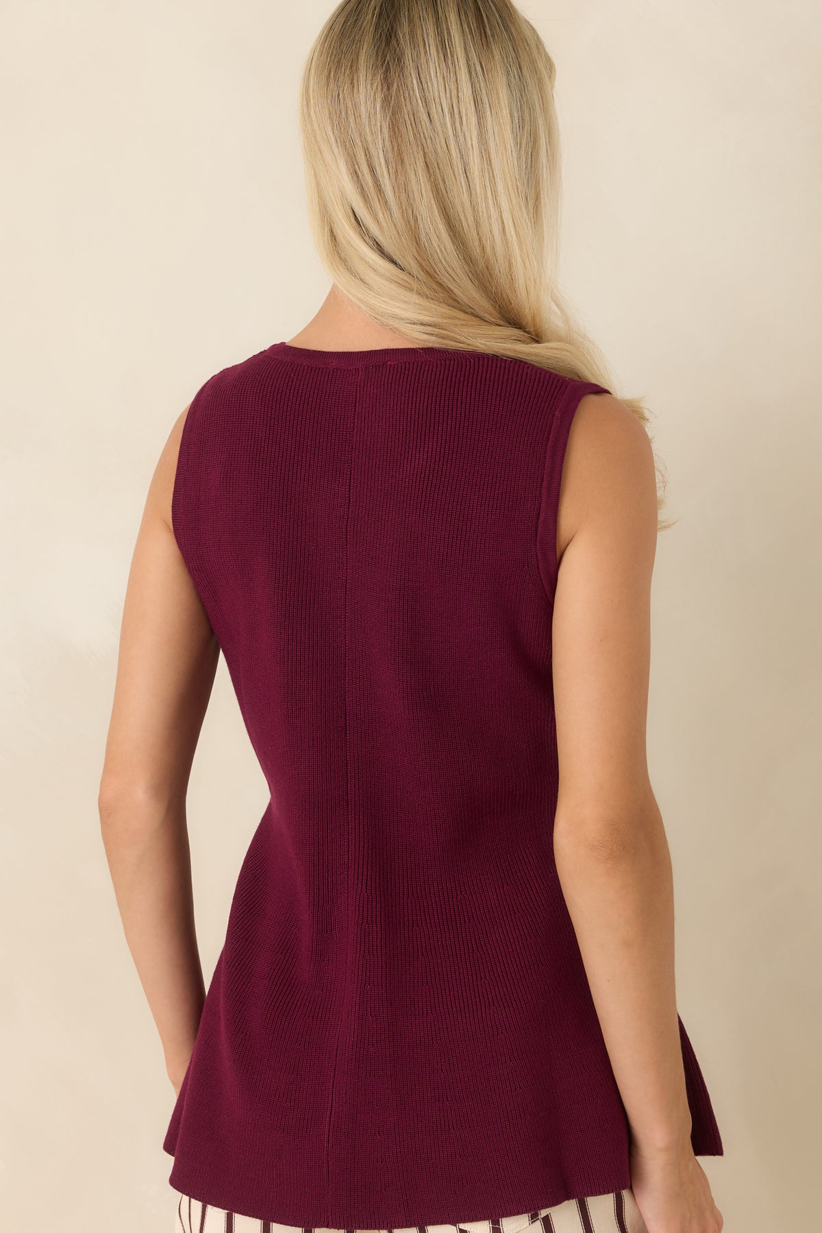 Back view of the sleeveless peplum top featuring a fitted shape, clean finish, and softly flared hemline.