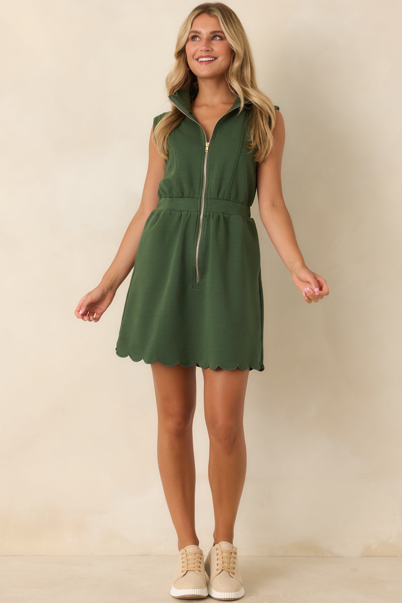 Sleeveless mini dress showcasing a structured silhouette, polished gold zipper, cap-style shoulders, and a scalloped finish along the hem.
