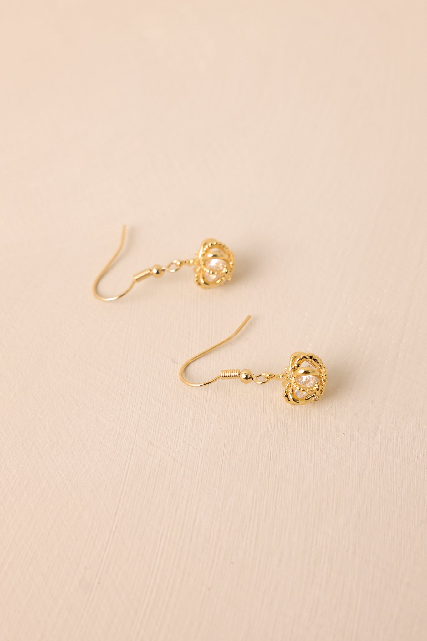 A slightly different angle of the earrings on a beige backdrop, emphasizing the gold hardware and dangling structure.