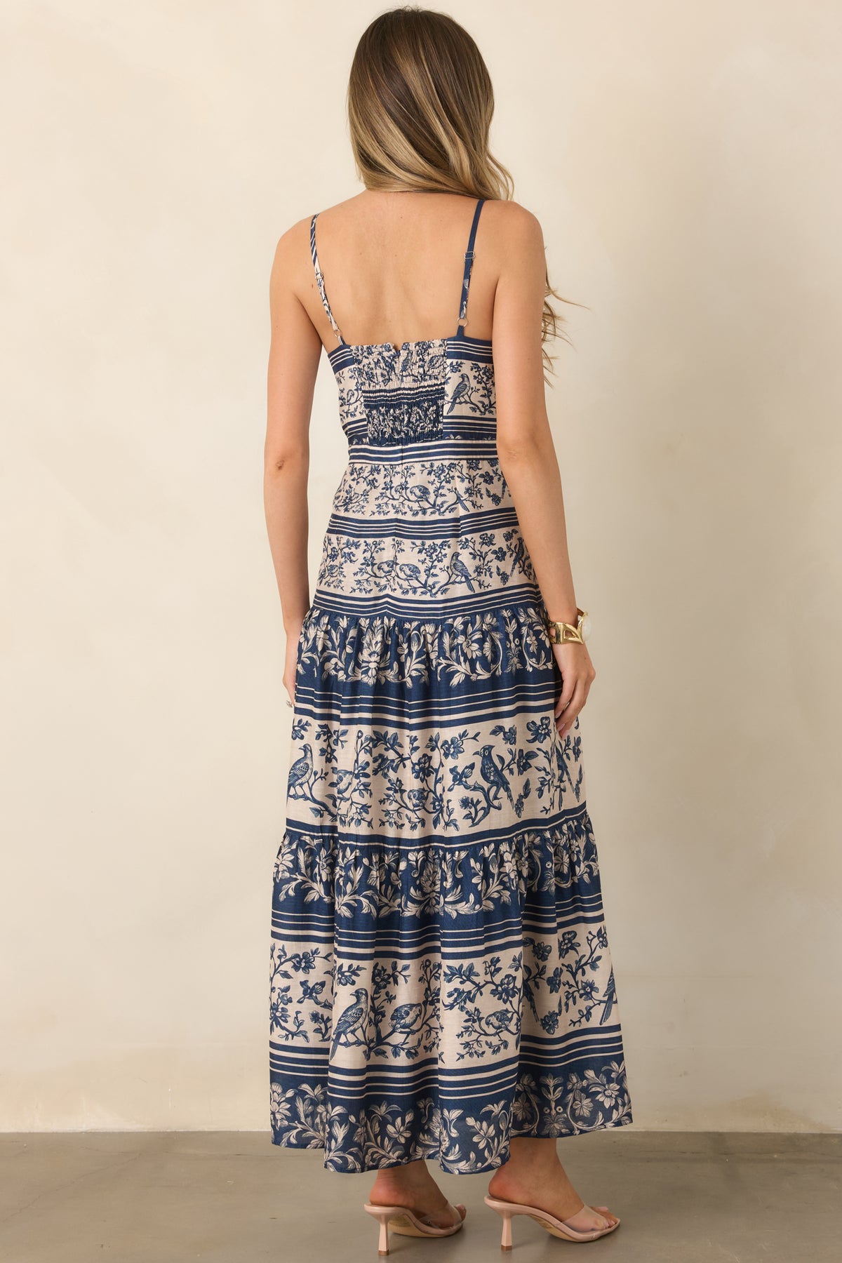 The rear of the dress features a smocked panel, concealed zipper, slender straps, and a full gathered tiered skirt.