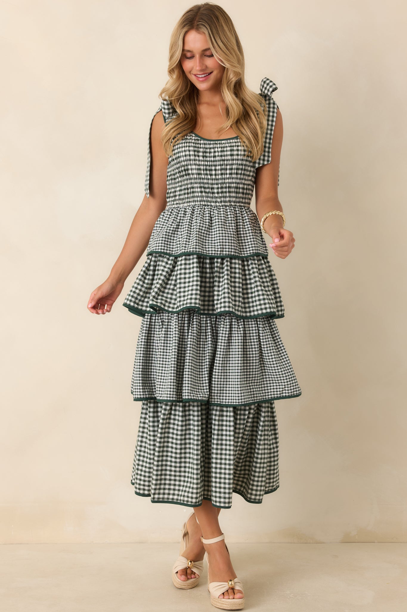Tiered dress featuring a smocked bodice, scoop neckline, fixed shoulder ties, elastic waist, and green trim.