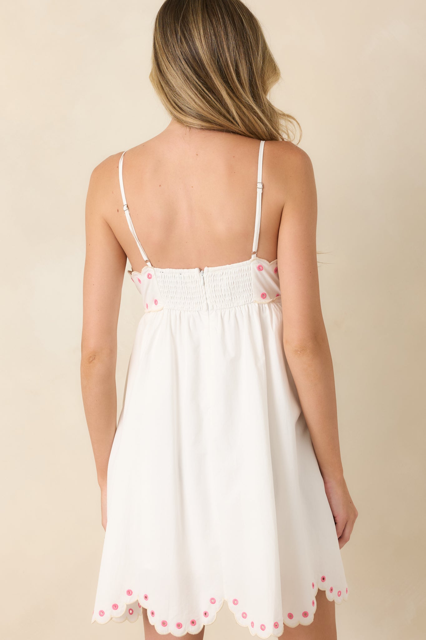 Rear view of the embroidered cotton mini dress featuring adjustable straps, a comfortable smocked back panel, and a scalloped embroidered hem.