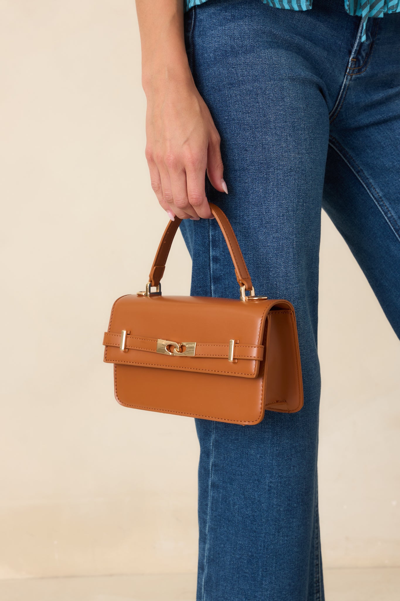 Smooth faux leather handbag showcasing an elegant top handle, adjustable shoulder strap, gold-tone accents, and a spacious structured design.