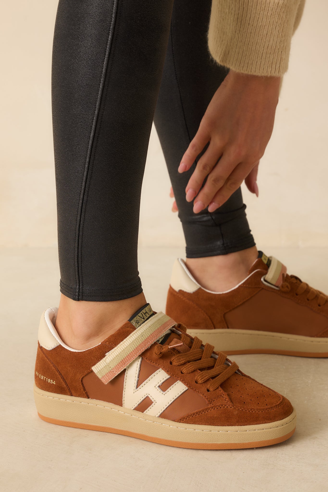 A close-up of the sneaker showing textured leather, smooth suede panels, and striped velcro strap details.