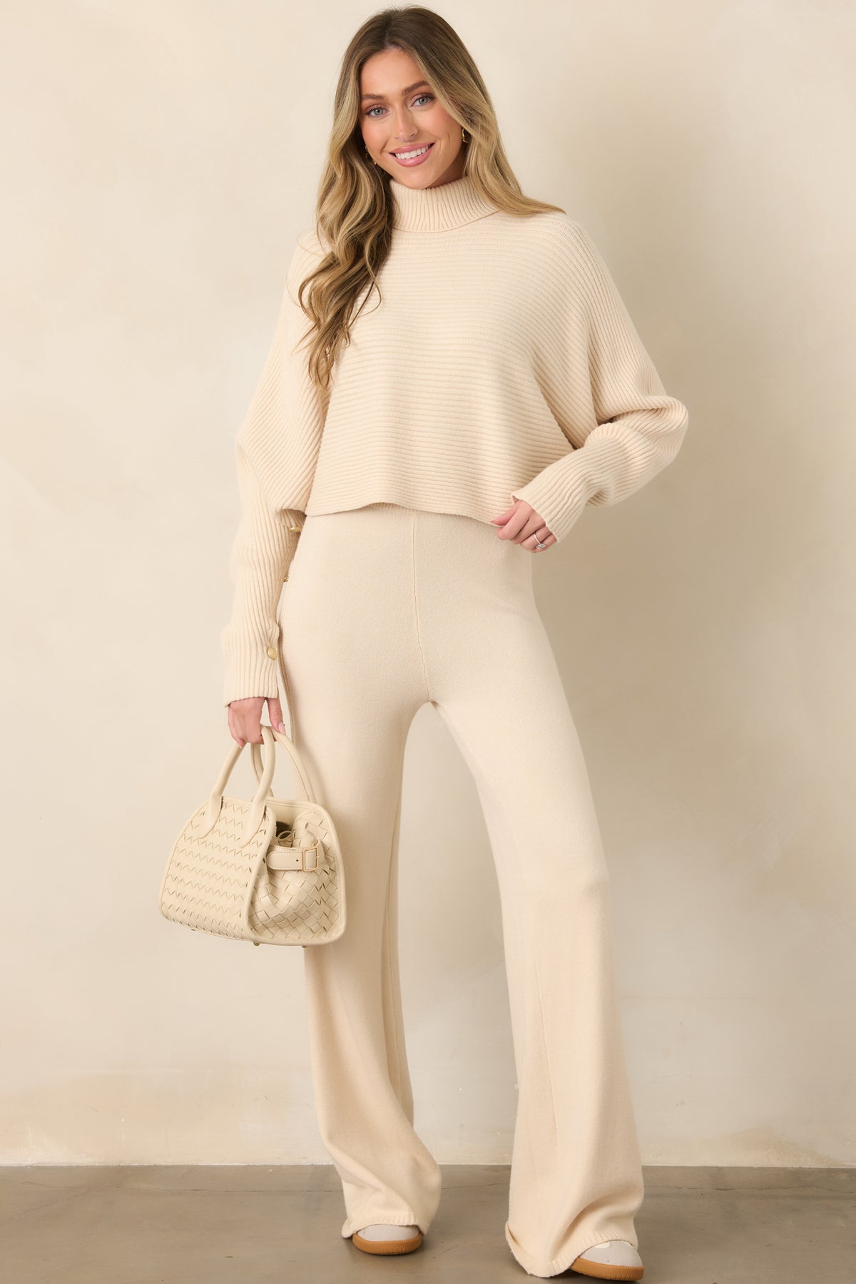 Soft beige ribbed sweater designed with a relaxed body, wide batwing sleeves, decorative cuff buttons, and a short, easy-wearing hem.