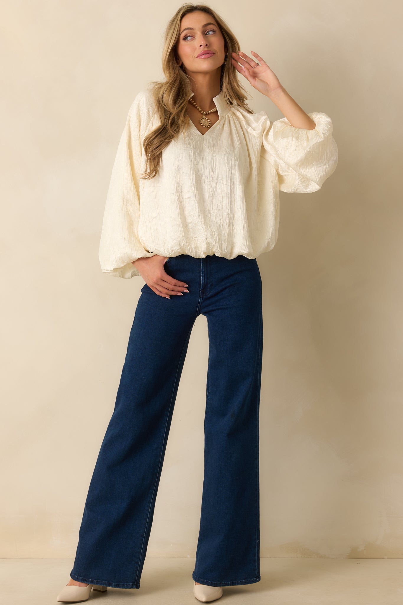 Soft cream top featuring a ruched neckline, flowing peasant sleeves, and a relaxed satin-finish fit.