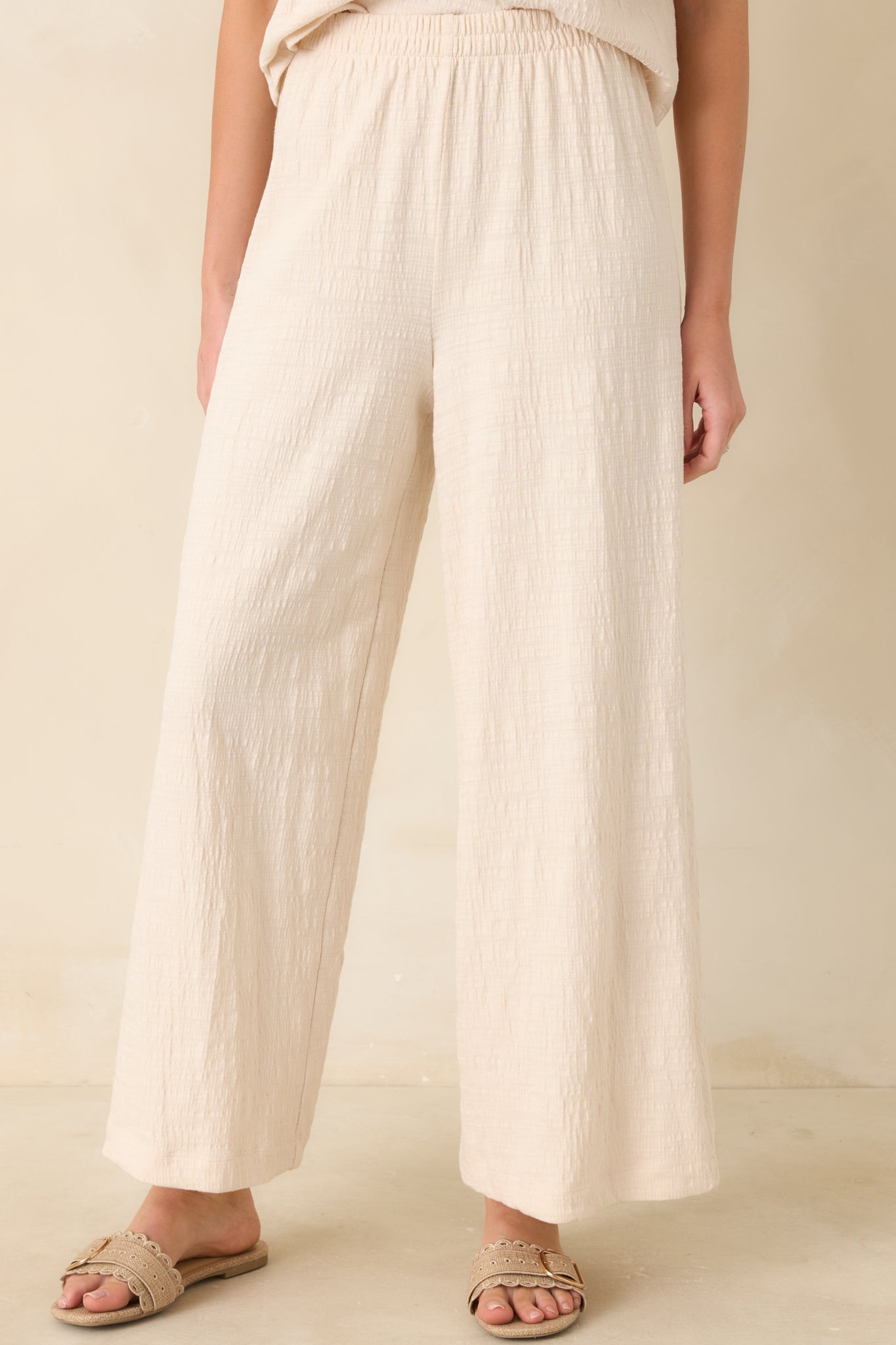 Soft crinkled fabric and wide-leg silhouette detail on ivory pants.