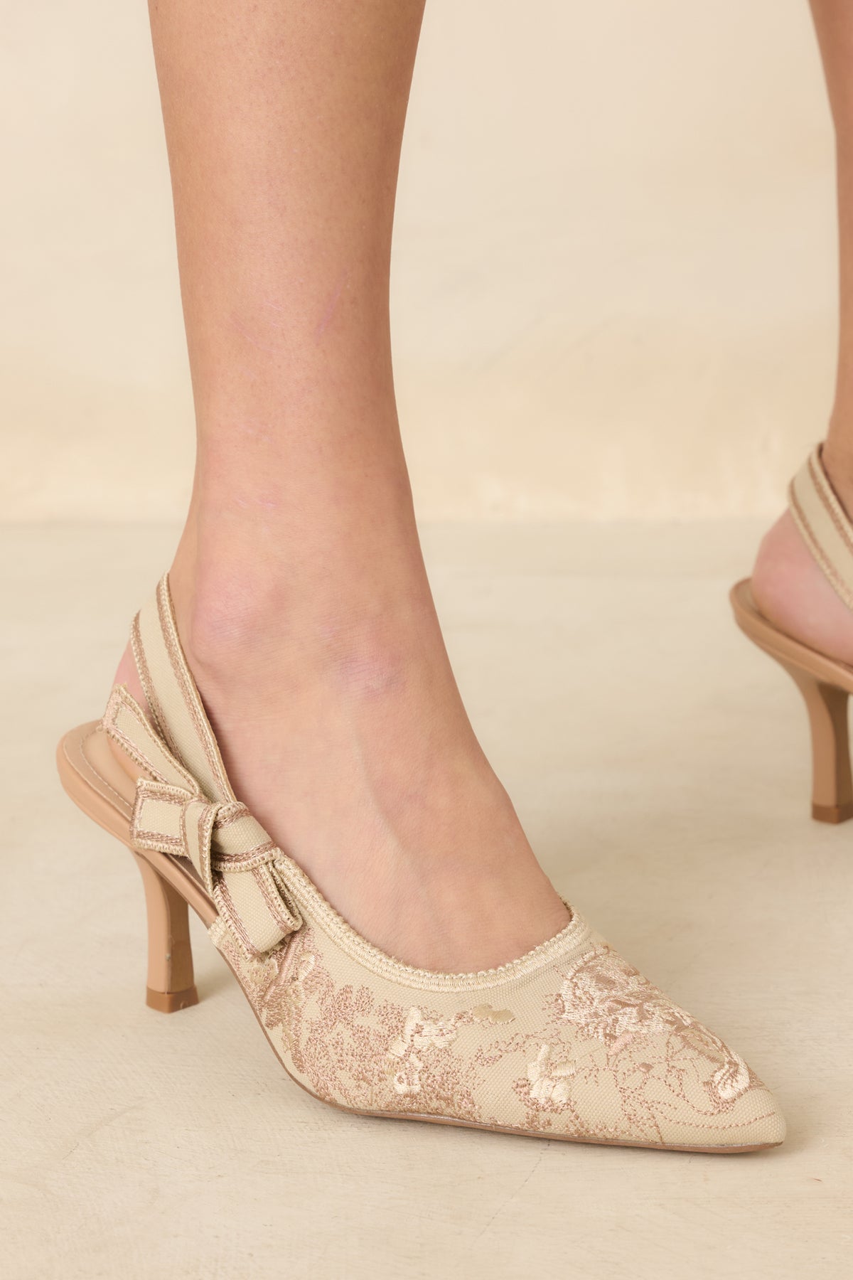 Soft gold slingback heels with pointed toes, embroidered fabric, contrast detailing, and mid-height heels.