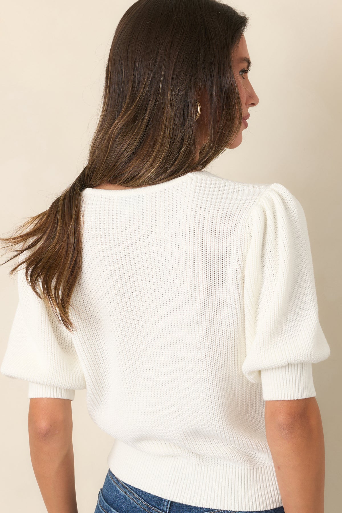 Rear of the soft ivory top featuring lightly gathered shoulders, puff sleeves, and a ribbed hem.