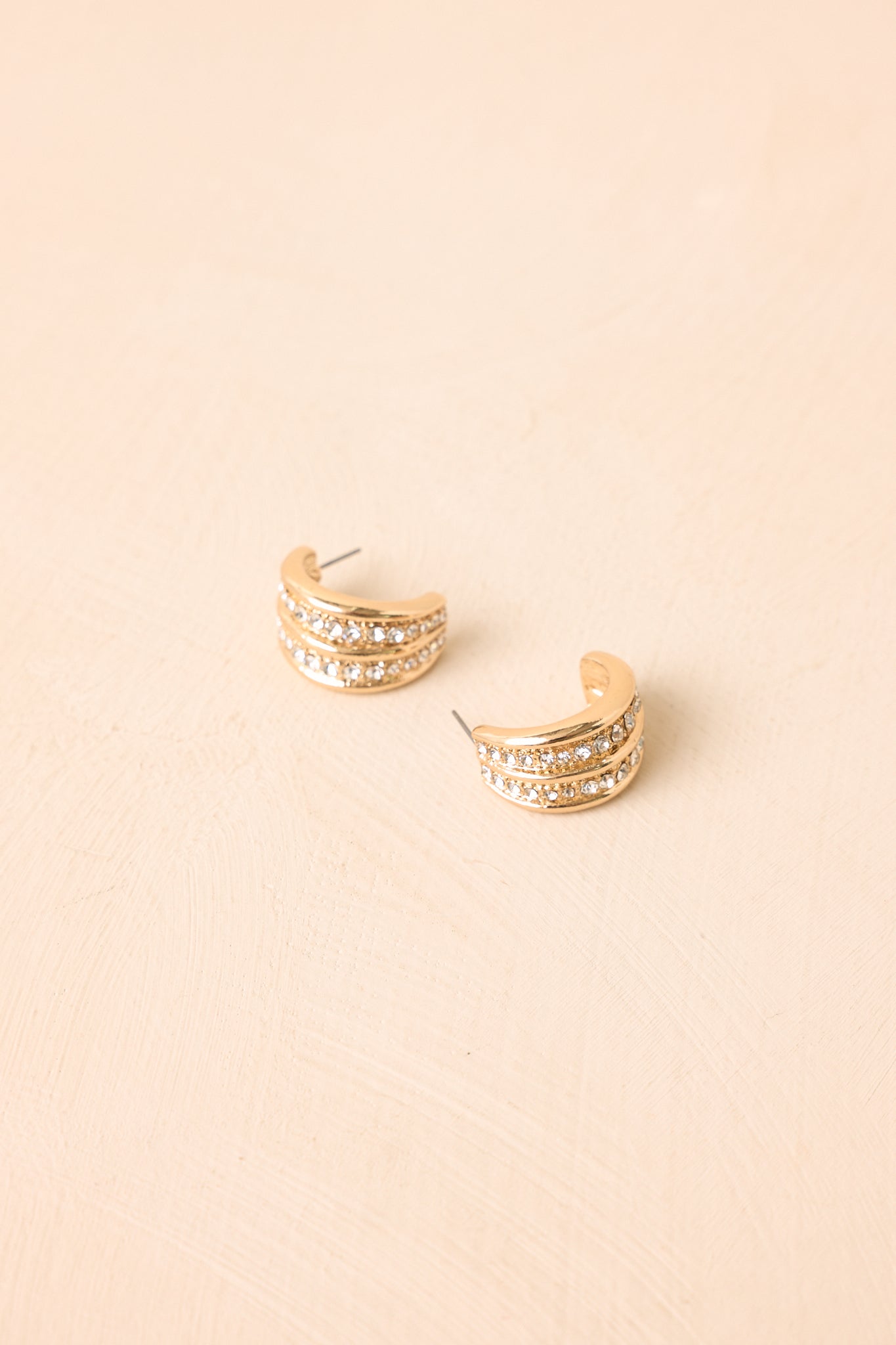 Softly rounded hoop earrings with a polished gold finish and sparkling crystal details presented on a neutral backdrop.