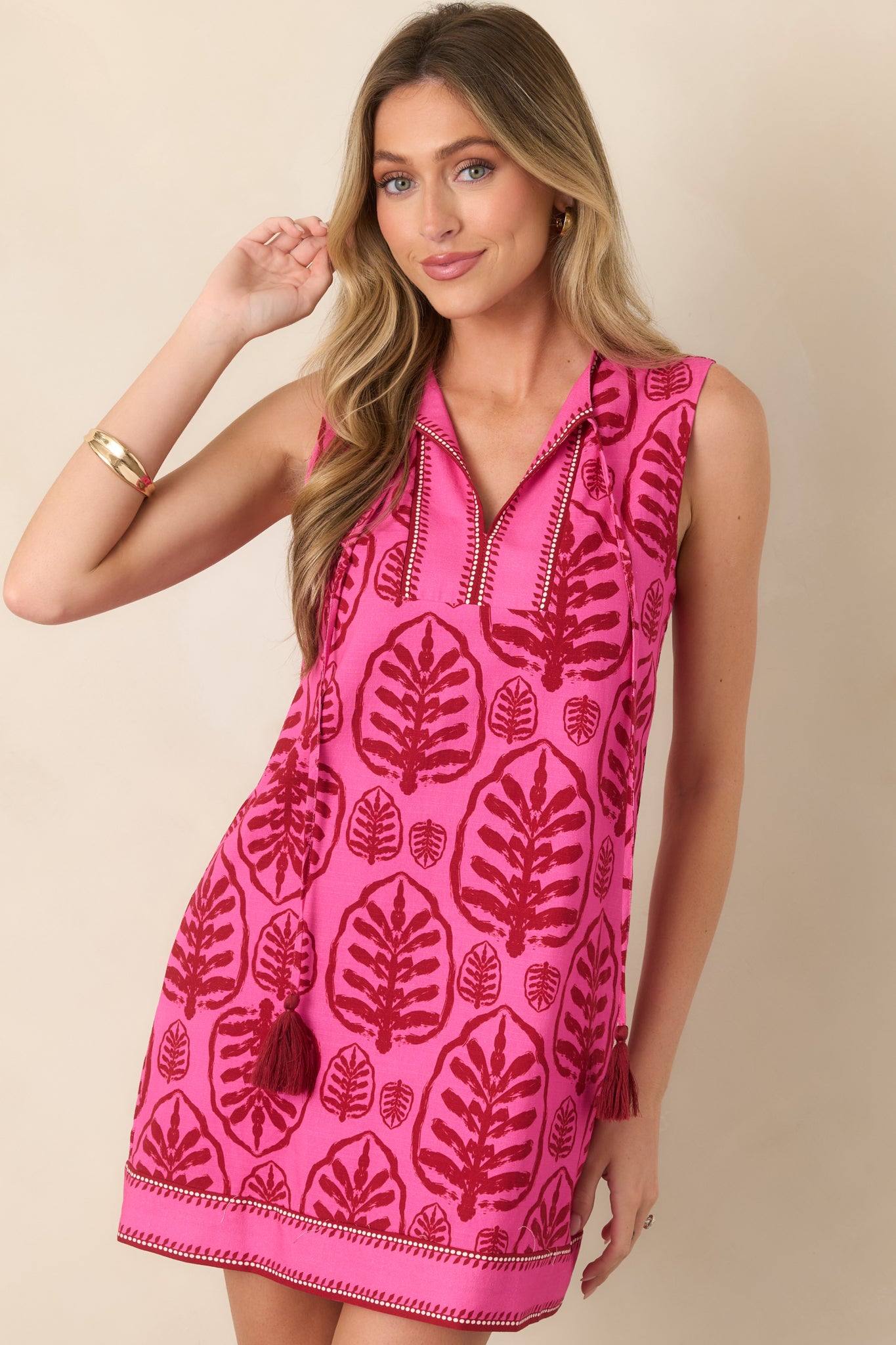 Close view of the mini dress’s split neckline and decorative contrast stitching, accented by long tasseled ties.