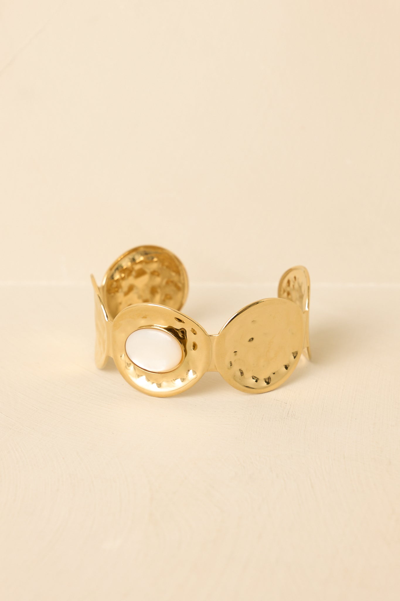 Front view of statement gold cuff with textured hammered segments and central polished circle set against neutral beige.