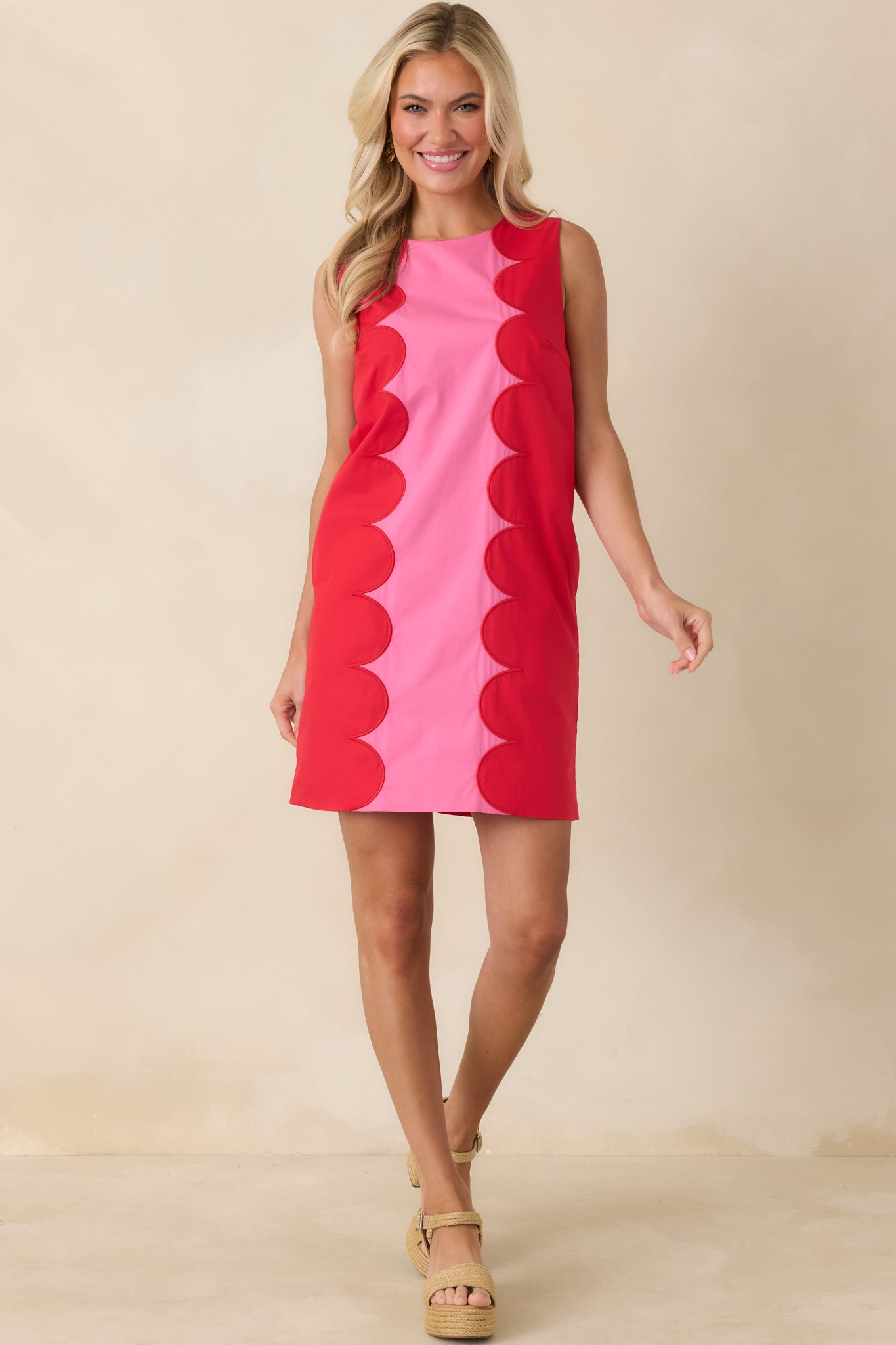Statement mini dress designed with a vivid pink center framed by red scalloped trim and a polished shape.