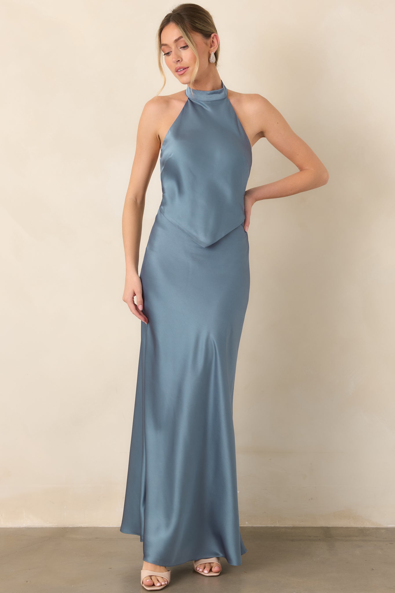 Steel blue satin gown displaying a polished halter neckline, dimensional bodice overlay, and elongated fluid skirt.